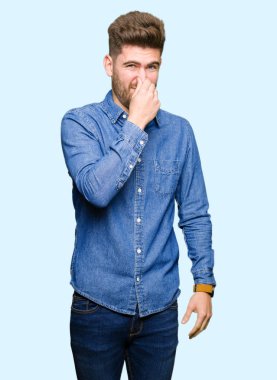 Rahat denim gömlek giyen genç yakışıklı sarışın adam bir şey kokmuş ve mide bulandırıcı, tahammül edilemez koku, burun üzerinde parmaklar ile nefes tutuyor. Kötü koku kavramı.
