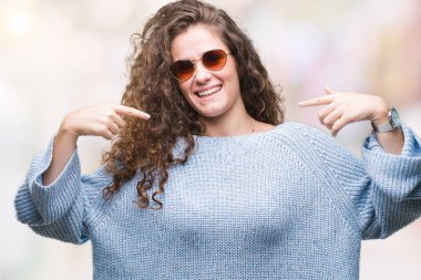 Yüzünde gülümseme ile kendinden emin görünüyorsun, kendini gururlu ve mutlu parmakları ile işaret izole arka plan üzerinde güneş gözlüğü takıyor güzel esmer kıvırcık saçlı Genç kız.