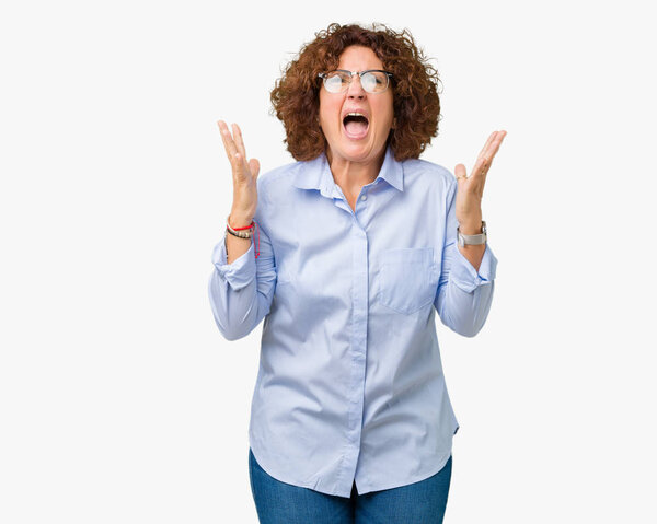 Beautiful middle ager senior businees woman wearing glasses over isolated background crazy and mad shouting and yelling with aggressive expression and arms raised. Frustration concept.