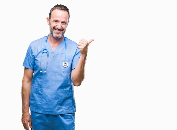 中年老人穿着医疗制服在孤立的背景微笑着快乐的脸看着 并指向侧面与拇指向上 — 图库照片