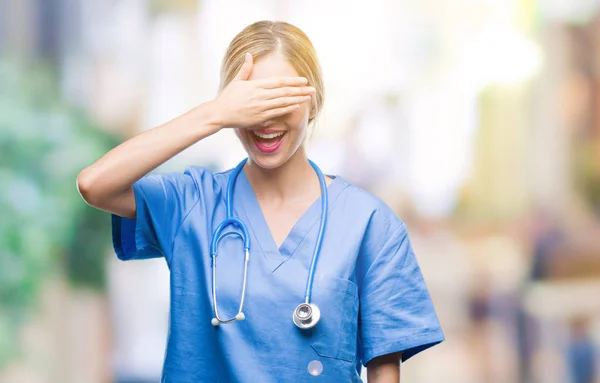 若い美しい金髪の医者の外科医看護師女性微笑し 笑う顔を驚きの目を覆って上の手で隔離された背景の上 視覚障害者の概念 — ストック写真