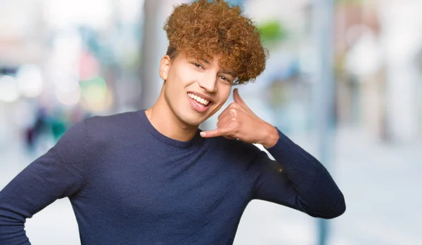 Young handsome man with afro hair smiling doing phone gesture with hand and fingers like talking on the telephone. Communicating concepts.