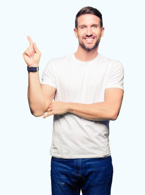 Yakışıklı adam, yüzünde kocaman bir gülümseme ile rahat beyaz t-shirt giyen kameraya bakarak yan el ve parmak ile işaret.