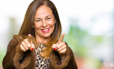 Sen ve kameraya gülümseyen pozitif ve neşeli parmaklarıyla işaret güzel orta yaş zarif kadın giyiyor vizon ceket