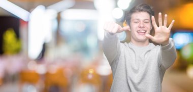 Gösterilen arka plan üzerinde sweatshirt giyen genç yakışıklı sportif adam izole ve parmakları ile işaret kendinden emin ve mutlu gülümseyerek süre 6 numara.