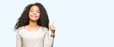 Rahat kazak giyen kıvırcık saçlı Genç güzel kız el ile jest kadar mutlu başparmak yapıyor. Başarı gösteren kameraya bakarak ifadeyi onaylama.
