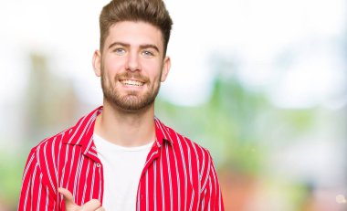 Kırmızı gömlek giyen genç yakışıklı adam el ile jest kadar mutlu thumbs yapıyor. Başarı gösteren kameraya bakarak ifadeyi onaylama.