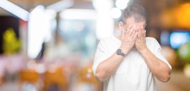 Orta yaş Arap adam wearig ağlayarak süre üzgün ifade ile yüz kapsayan ile izole arka plan üzerinde beyaz t-shirt eller. Depresyon kavramı.