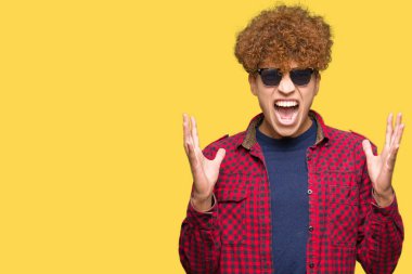 Yakışıklı genç afro saçlı deli ve deli bağırarak ve agresif ifade ve silah kaldırdı bağırmaya güneş gözlüğü takıyor. Hayal kırıklığı kavramı.
