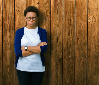 İzole arka plan şüpheci ve çapraz kolları olan yüzündeki gergin, onaylamayan ifade gözlüklü genç güzel Afrikalı-Amerikalı kadın. Negatif kişi.