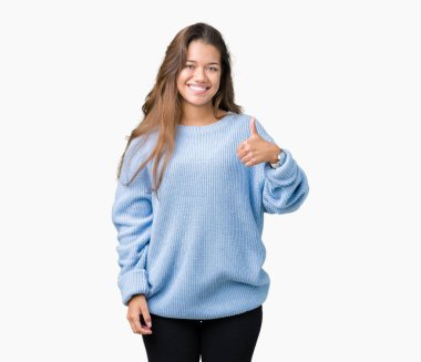 Genç güzel esmer kadın el ile jest kadar mutlu başparmak yapıyor izole arka plan üzerinde mavi kış kazak giyiyor. Başarı gösteren kameraya bakarak ifadeyi onaylama.