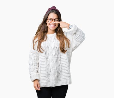 Genç güzel esmer hipster kadın gözlük ve kış şapka izole üzerinde işaretleme için yüz ve burun, neşeli gülümseyerek el parmak ile arka plan