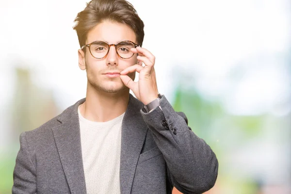 Young business man wearing glasses over isolated background mouth and lips shut as zip with fingers. Secret and silent, taboo talking