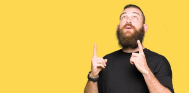 Rahat t-shirt giyen genç sarışın adam hayret ve yukarıya bakıyor ve parmakları ile işaret ve silah kaldırdı şaşırttı.