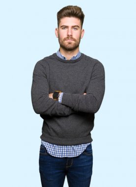 Genç yakışıklı zarif adam şüpheci ve sinir, kesişmiş silah ile yüz ifade onaylamıyor. Negatif kişi.