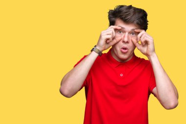 İzole arka planda kırmızı tişört giyen genç yakışıklı adam parmaklar, Uykulu ve sabah yorgunluk için yorgun gözleri açmaya çalışıyor