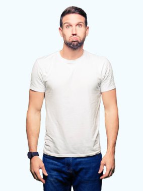 Komik surat ile rahat beyaz t-shirt şişirme yanakları giyen yakışıklı adam. Ağız ile hava, deli ifade şişirilmiş.
