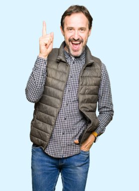 Orta yaş yakışıklı adam kış yelek işaret parmağı ile başarılı fikir giyiyor. Çıktıktan ve mutlu. Bir numara.