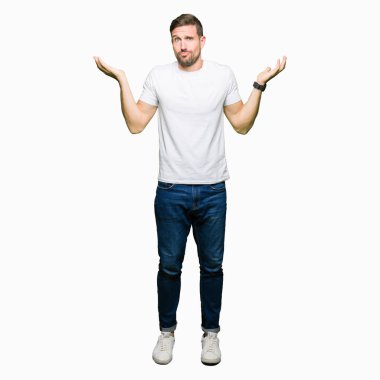 Yakışıklı adam rahat beyaz t-shirt clueless ve şaşkın bir ifadeyle kollar ve eller kaldırdı giyiyor. Şüphe kavramı.