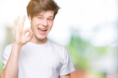 İzole arka plan el ve parmaklar ok işaretiyle yapıyor olumlu gülümseyen üzerinde rahat beyaz t-shirt giyen genç yakışıklı adam. Başarılı ifade.