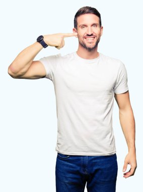 Neşeli gülümseyen casual beyaz t-shirt işaretçi el parmak yüz ve burun, giyen yakışıklı adam