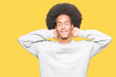 Sportif sweatshirt giyen afro saçlı genç Afro-Amerikan adam rahatlatıcı ve kollar ve eller baş ve boyun, mutlu gülümseyerek arkasında ile germe