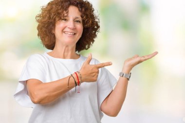 Hayret ve el ile sunulması ve parmak ile işaret ederken kameraya gülümseyen izole arka plan üzerinde beyaz t-shirt giyen kadın güzel orta ager kıdemli.