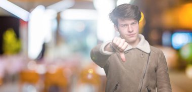 Genç yakışıklı adam mutsuz ve kızgın ret gösterilen ve başparmak aşağı hareketi ile negatif seyir izole arka plan üzerinde kış palto giyiyor. Kötü ifade.