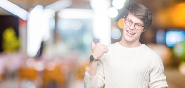 Seyir ve başparmak yanında yukarıyı mutlu yüz ile gülümseyen izole arka plan üzerinde gözlük takan genç yakışıklı adam.