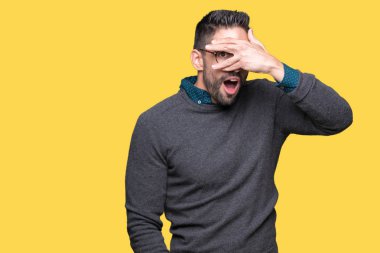 Mahcup ifadeyle parmaklarımın arasından seyir yüz ve gözler el ile kapsayan şok bakmak izole arka plan üzerinde gözlük takan genç yakışıklı adam.