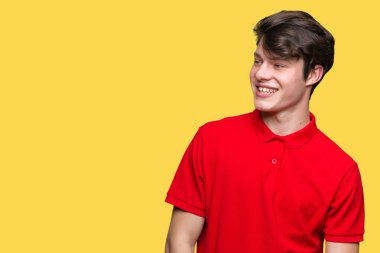 Uzak tarafına yüzünde, doğal ifade gülümseme ile seyir izole arka plan üzerinde kırmızı t-shirt giyen genç yakışıklı adam. Kendine güvenen gülüyor.