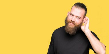 Rahat t-shirt el ile gülümseyen bir işitme söylenti ya da dedikodu için dinleme kulak üzerinde giyen genç sarışın adam. Sağırlık kavramı.