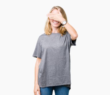 Güzel genç kadın büyük boy rahat t-shirt üzerinde izole arka plan gülümseyen ve sürpriz için gözleri kapsayan yüzünde el ile gülüyor giyiyor. Kör kavram.