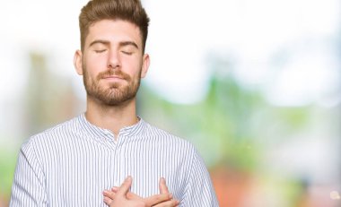 Elleri göğsünde, gözleri kapalı gülümseyen ve yüzünde minnet ifadesi olan genç yakışıklı bir adam. Sağlık kavramı.
