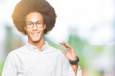 Afrikalı-Amerikalı genç afro saçlı gözlüklü büyük ve büyük boy işaret, ölçü birimi sembol gösteren elleriyle işaret. Kameraya bakarak gülümsüyordu. Ölçüm kavramı.