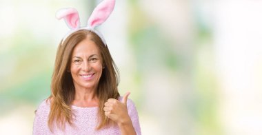 Paskalya tavşan kulakları hareketi el ile mutlu yaşasın yapıyor izole arka plan üzerinde giyen orta yaş esmer kadın. Kameraya bakarak başarı gösteren ile ifade onaylama.