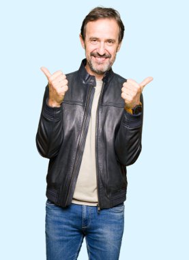 Siyah deri ceket başarı işareti giyen orta yaş yakışıklı adam el ile olumlu jest yapıyor, gülümseyen ve mutlu kadar başparmak. Neşeli ifade ile kamera bakarak, kazanan jest.