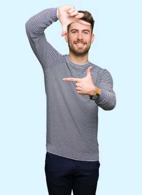 Yakışıklı delikanlı giyen kazak gülümseyen yapım çerçeve elleri ve parmakları ile mutlu yüz çizgili. Yaratıcılık ve Fotoğrafçılık kavramı.