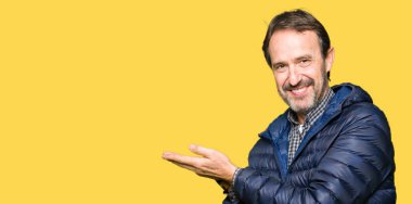 Orta yaş yakışıklı adam giyen kış işaretçi el yanında kat ve açık palm, mutlu ve kendine güvenen reklam gülümseyen sunulması