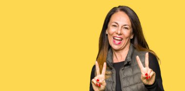 Zafer işareti yapıyor parmak gösterilen kamera seyir gülümseyen güzel orta yaş kadın giyiyor kış yelek. İki numaralı.