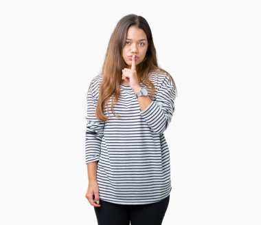 Dudaklarında parmak ile sessiz olmanı izole arka plan üzerinde çizgili süveter giyen genç güzel esmer kadın. Sessizlik ve gizli kavramı.