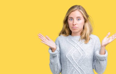 İzole arka plan clueless ve şaşkın bir ifadeyle kollar ve eller kaldırdı üzerinde kış kazak giyen güzel genç kadın. Şüphe kavramı.