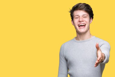 Üzerinde kış kazak giyen genç yakışıklı adam arka plan dostu sunan karşılıklı tebrik ve davet edici gülümseyen izole. Başarılı iş.