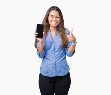 Genç güzel esmer iş kadın büyük bir gülümseme ile izole arka plan üzerinde akıllı telefon ekranını gösteren ok işareti, parmak yukarı başparmak, mükemmel işareti yapıyor