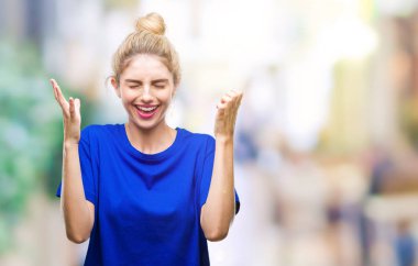 Kızgın ve silah ile başarı için deli izole arka plan kutluyor üzerinde mavi t-shirt giyen genç güzel sarışın ve mavi gözlü kadın kaldırdı ve heyecanlı çığlık gözler kapalı. Kazanan kavramı