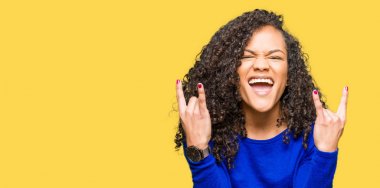 Kıvırcık saçlı Genç güzel kadın, eller yukarı kaya sembolü yapan çılgın ifade ile bağırarak kış kazak giyiyor. Müzik yıldızı. Ağır kavram.