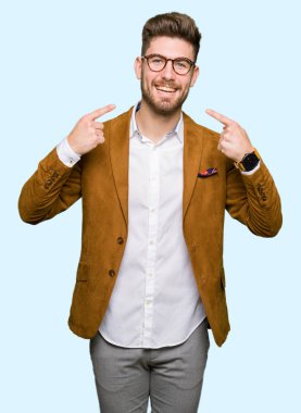 Kendinden emin gösterilen ve işaret parmakları diş ve ağız ile gülümseyen gözlüklü genç yakışıklı iş adamı. Sağlık kavramı.