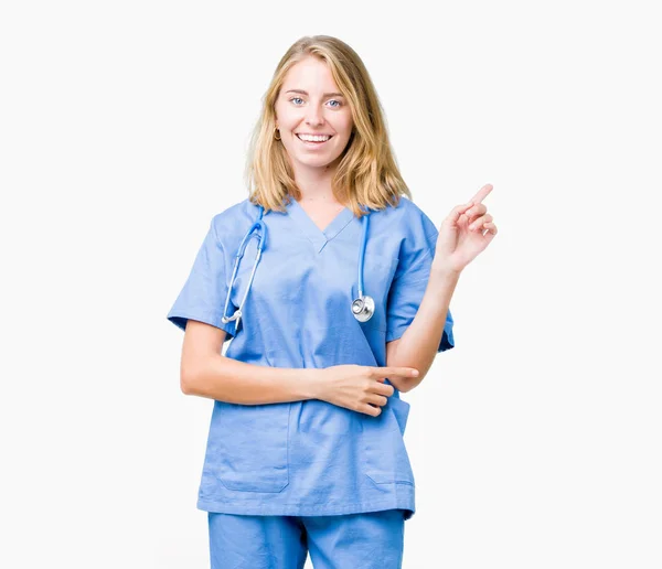 顔に大きな笑顔で孤立した背景の上に医療の制服を着た美しい若い医師の女性は カメラを見ている側に手と指で指して — ストック写真