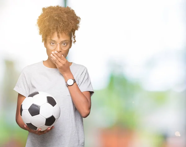 Young african american woman holding soccer football ball over isolated background cover mouth with hand shocked with shame for mistake, expression of fear, scared in silence, secret concept