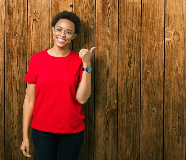 Güzel genç Afro-Amerikan kadın arıyorum ve başparmak yanında yukarıyı mutlu yüz ile gülümseyen izole arka plan üzerinde gözlük.